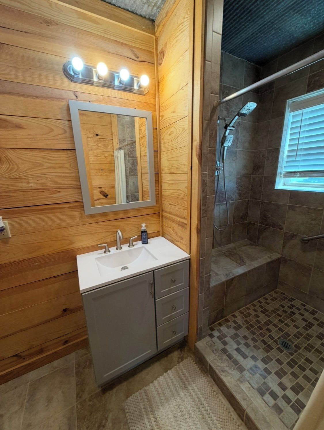 A bathroom with wooden walls, a white sink, a mirror, and a shower area.
