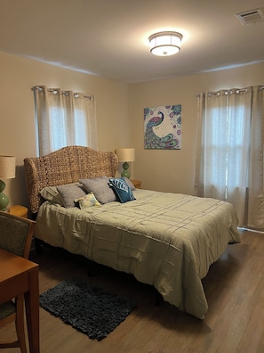 A bedroom with a bed, a nightstand, a lamp, a chair, a rug, and a wall painting.