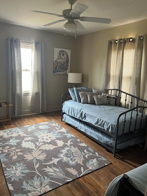 A bedroom with a bed, a ceiling fan, a window with curtains, a wall-mounted lamp, and a floral-patterned rug. - Mae Cottage Cozy 3-bedroom cottage near Douglas, GA - Pet friendly (Douglas)