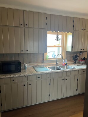 A kitchen with white cabinets, a microwave, a sink, and a window with a view of the outside. - Mae Cottage Cozy 3-bedroom cottage near Douglas, GA - Pet friendly (Douglas)