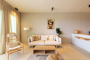 Un salon comprenant un canapé, un fauteuil, une table basse, un lampadaire et un tableau accroché au mur.