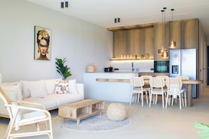 A modern kitchen with wooden cabinets, a dining area with wicker chairs, and a white sofa. - Solara - Luxury 3-Bedroom Home with Private Pool (Willemstad)