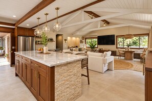 A spacious kitchen with a large island, wooden cabinets, and a stone accent wall. - Kona Gathering Home | Sunset Views, Lanai & BBQ (Kailua-Kona)