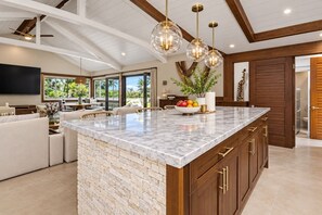 A spacious kitchen with a large island, wooden cabinets, and pendant lighting. - Kona Gathering Home | Sunset Views, Lanai & BBQ (Kailua-Kona)