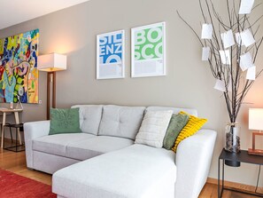 Een moderne woonkamer met een lichtkleurige modulaire bank, een kleurrijk abstract schilderij en twee ingelijste documenten aan de muur.