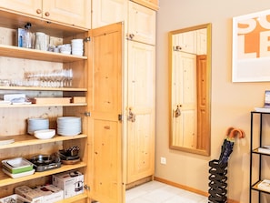 Une cuisine avec des meubles de rangement en bois, des étagères où sont disposés de la verrerie, des assiettes et des ustensiles de cuisine.