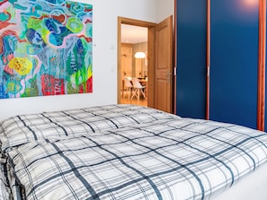 A bedroom with a bed, a colorful abstract painting, and a view into a dining area. - Chesa Altrova by Interhome (St. Moritz)