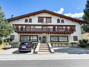 Ein zweistöckiges Gebäude mit Balkon, ein Auto davor und ein klarer Himmel.