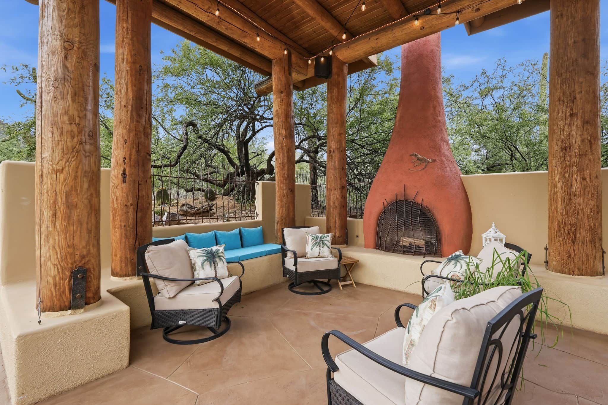 An outdoor patio with wooden pillars, a stone fireplace, and outdoor furniture.
