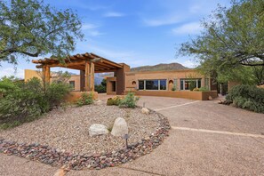 A modern building with a covered patio, surrounded by a gravel driveway and landscaped garden with rocks and desert plants. - The Retreat
at Bear Canyon (Tanque Verde)