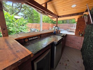 Ein Außenbereich mit einer Küche, einer Holztresore, einer integrierten Spüle und einem Grill.