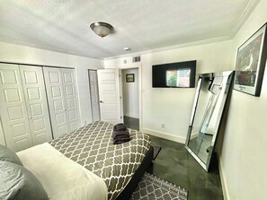 Ein Hotelzimmer mit einem Bett, einem Flachbildfernseher, einem Spiegel und einer Tür zu einem anderen Raum.