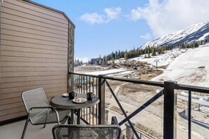 Ein Balkon mit Tisch und Stühlen, mit Blick auf eine verschneite Berglandschaft und eine Baustelle.