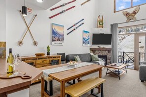 Uma sala de estar acolhedora com lareira, um espaço de jantar com mesa de madeira e equipamentos de esqui na parede.