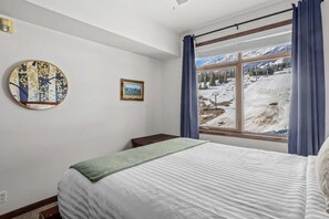 Um quarto com cama, janela com vista para uma paisagem nevada e duas decorações de parede.