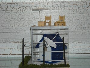 Maquete de um edifício com janela, interior azul e branco, e uma pequena área verde na base.