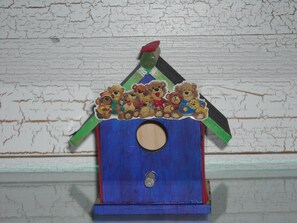 Uma casinha de pássaros de madeira com base azul e teto verde, decorada com adesivos de ursinhos de pelúcia.