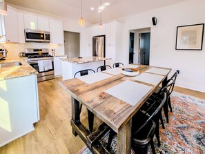 Een moderne keuken met witte kasten, roestvrijstalen apparatuur en een houten eettafel met stoelen.