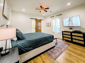 Ein Schlafzimmer mit einem Bett, einem Schminktisch, einem Deckenventilator, einem Fernseher und einer Tür.