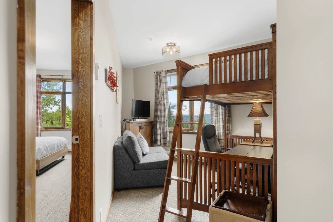 A room with a bunk bed, a sofa, a television, and a table with a lamp.