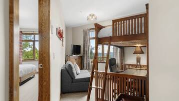 A room with a bunk bed, a sofa, a television, and a table with a lamp.