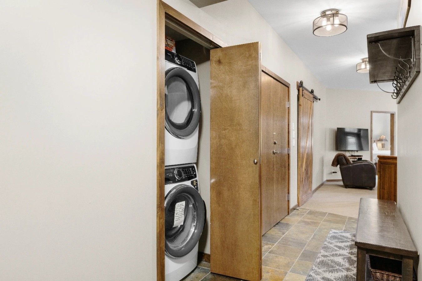 Une buanderie équipée d’un lave-linge et d’un sèche-linge, avec une porte en bois, un téléviseur et un coin salon comprenant un banc.