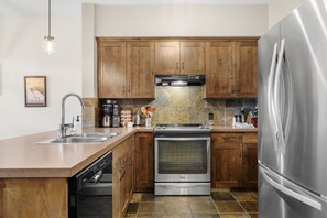 A modern kitchen with wooden cabinets, stainless steel appliances, and a dishwasher. - Golden Alpine Escape 3BR+Den HotTub+Ski In/Out (Golden)