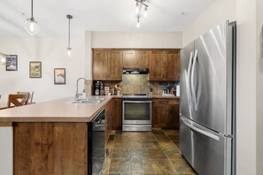 A modern kitchen with wooden cabinets, stainless steel appliances, and a central island. - Golden Alpine Escape 3BR+Den HotTub+Ski In/Out (Golden)