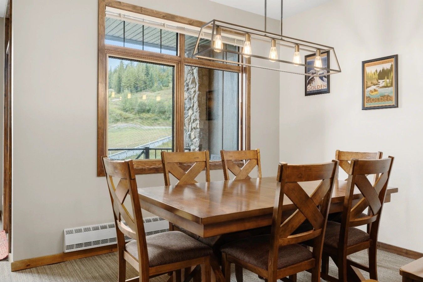 Un espace repas avec une table et des chaises en bois, de grandes fenêtres donnant sur un paysage verdoyant et un luminaire suspendu.