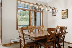 A dining area with a wooden table and chairs, large windows with a view of greenery, and a pendant light fixture. - Golden Alpine Escape 3BR+Den HotTub+Ski In/Out (Golden)