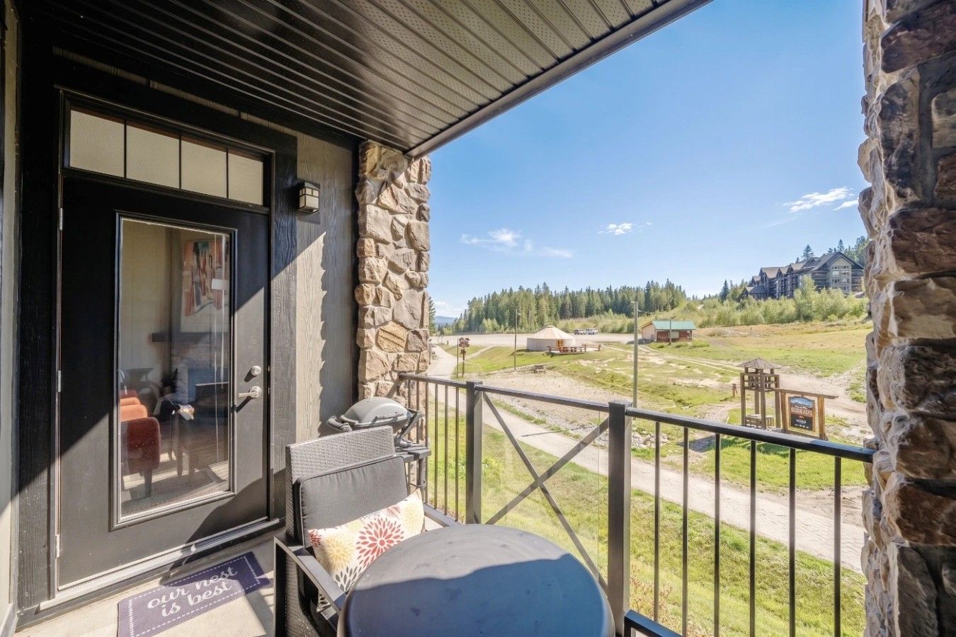 A balcony with a stone wall, a door, and a view of a rural landscape including a yurt and buildings.