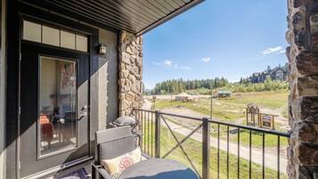 A balcony with a stone wall, a door, and a view of a rural landscape including a yurt and buildings.