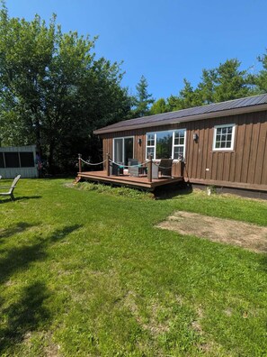 A wooden cabin with a deck, large windows, and a fenced outdoor area. - Short walking distance to beach. With fire pit, BBQ,n pedal boat. (Beaubassin-est)