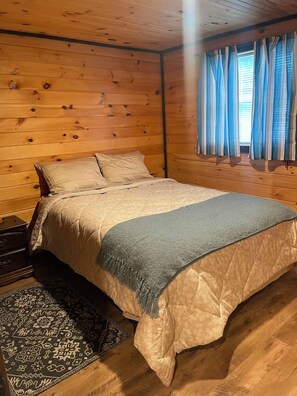 A wooden-paneled bedroom with a bed, pillows, a rug, and curtains.