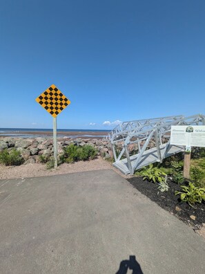 A paved path leading to a beach with a caution sign, a metal staircase, and a welcome sign.