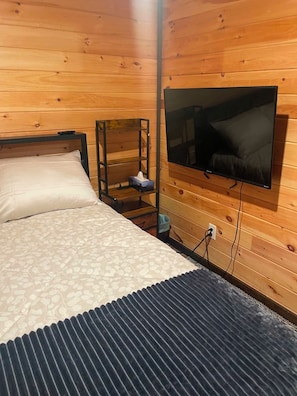A room with a bed, a TV mounted on the wall, and a wooden floor. - Short walking distance to beach. With fire pit, BBQ,n pedal boat. (Beaubassin-est)