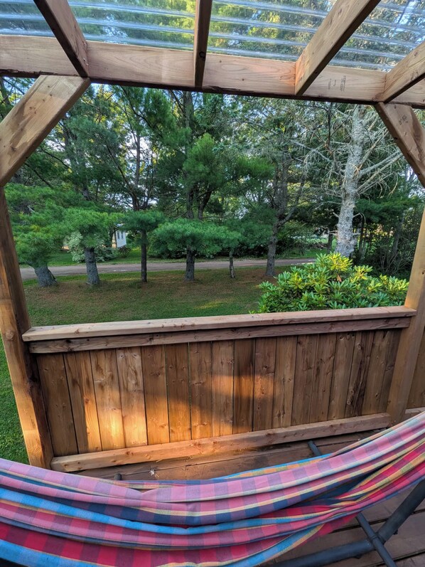 A wooden deck with a hammock and a view of a landscaped garden with various trees and shrubs.