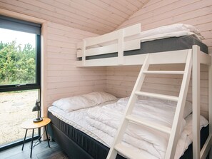 A bunk bed with a ladder, a small table with a lamp, and a window with a view of greenery. - 5 Star Holiday Home in Romo (Rømø)