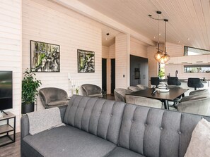 A modern living room with a grey sofa, dining table, and chairs, wooden panel walls, and artwork. - 5 Star Holiday Home in Romo (Rømø)