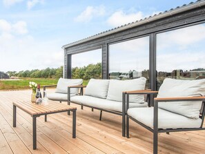 A deck with a sofa and a table, large windows, and a view of the countryside. - 5 Star Holiday Home in Romo (Rømø)