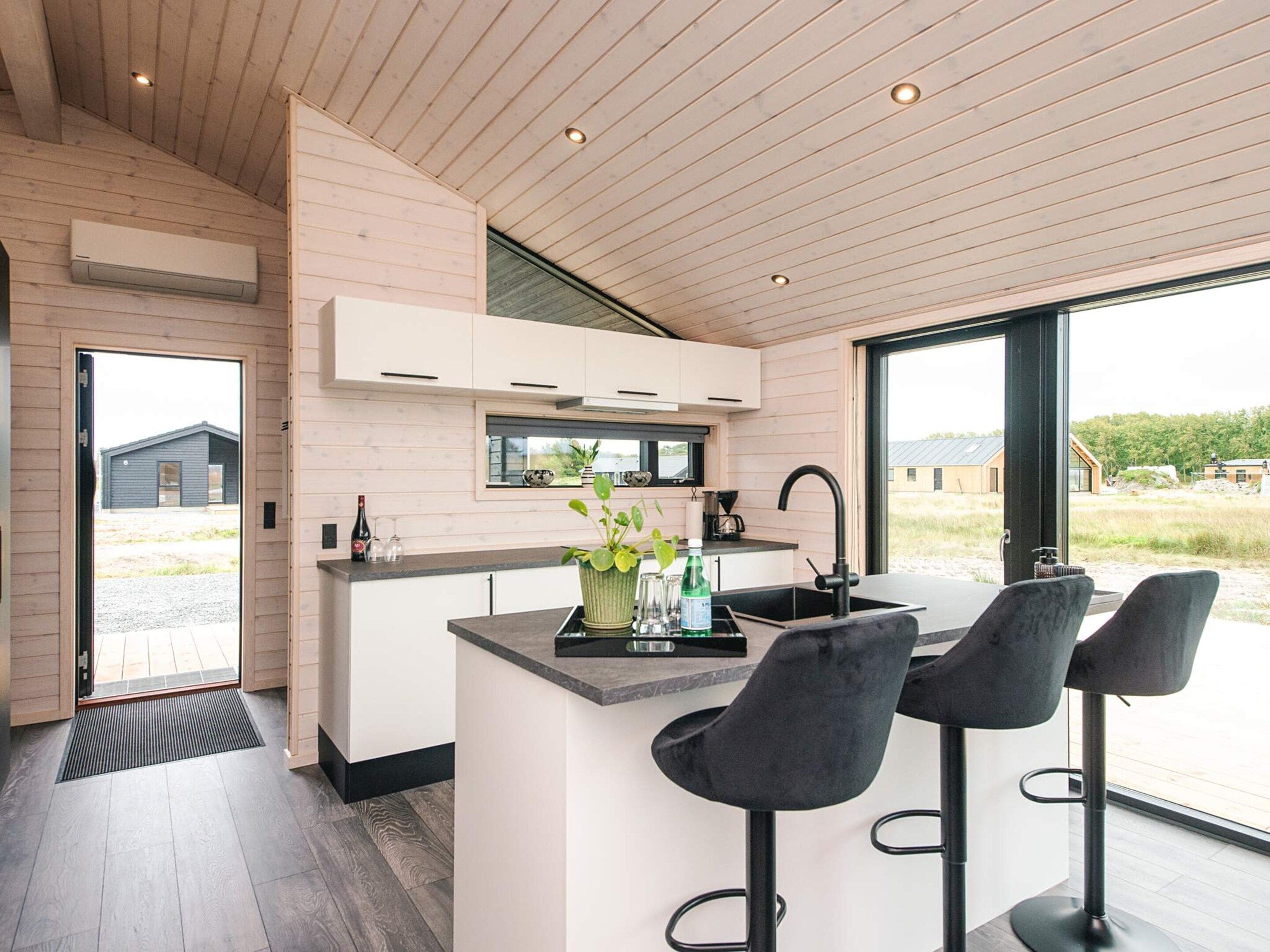 A modern kitchen with a central island, bar stools, and a large window offering a view of the outdoors.