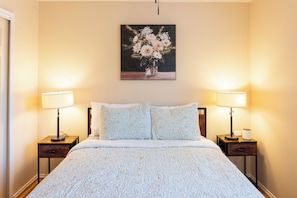 Une chambre d’hôtel avec un lit, deux lampes de chevet, une table de nuit, un oreiller et un tableau représentant des fleurs accroché au mur.