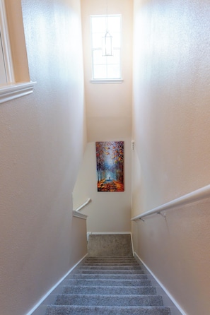 Una escalera alfombrada con barandilla, un cuadro en la pared y una ventana en la parte superior.