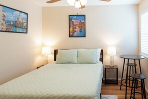 Une chambre d’hôtel avec un lit, deux lampes de chevet, une petite table avec une chaise et deux tableaux au mur.