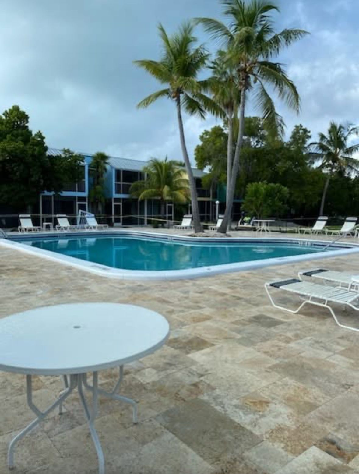 A swimming pool with lounge chairs and a table, surrounded by palm trees and a building.