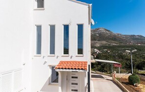 A white building with a red-tiled roof, multiple windows, and a view of a mountainous landscape. - 1 bedroom nice apartment in Cavtat (Cavtat)