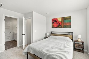 Un dormitorio con cama, mesitas de noche, un armario auxiliar, una puerta y una pared decorada con una pintura floral.