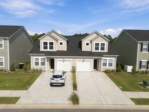 A two-story residential building with a garage, a driveway, and a parked car. - Brilliant 3-bedroom house with AC near ocean Isl Bch (OCEAN ISL BCH)