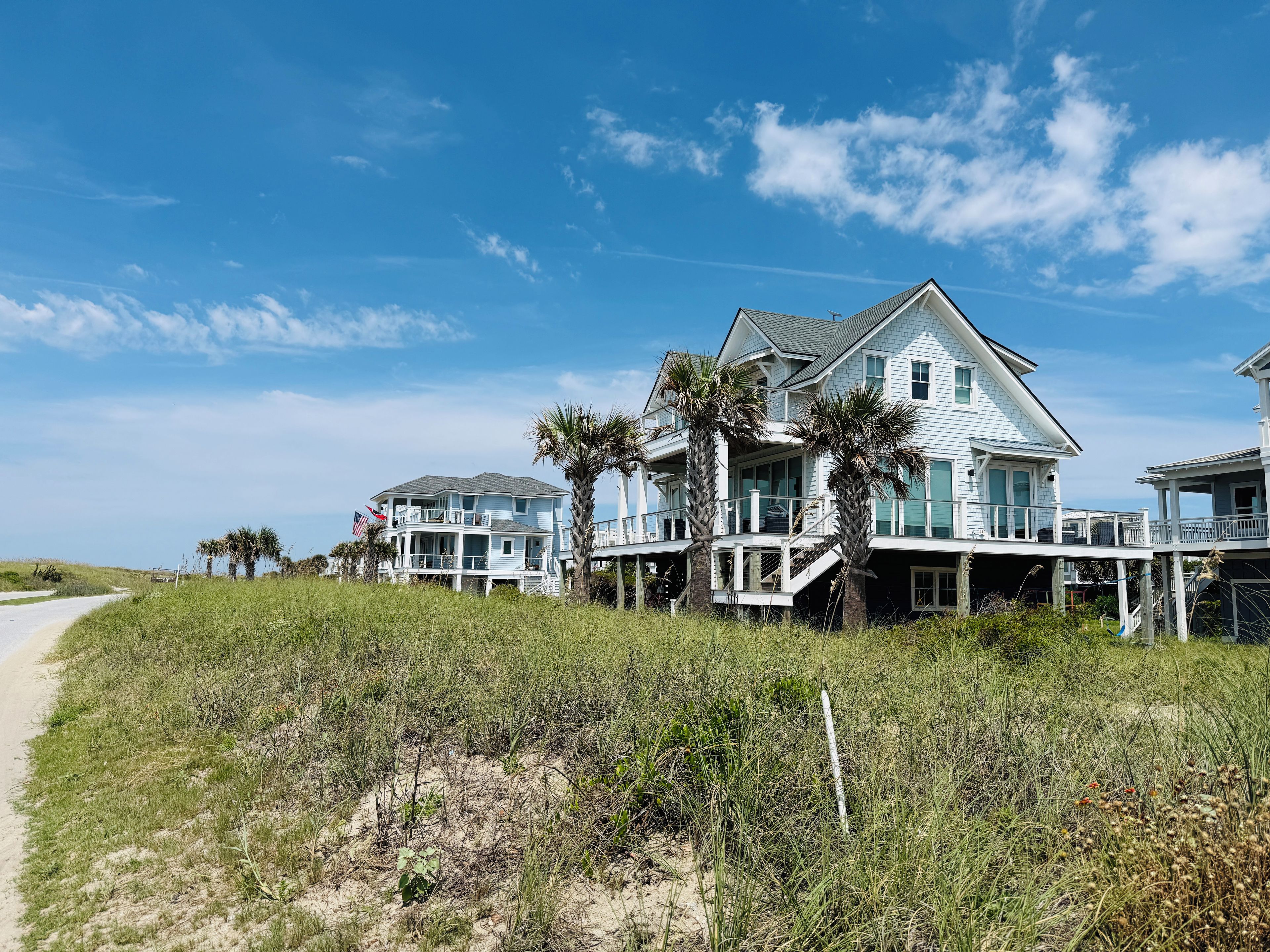 Une propriété située en bord de mer, avec des maisons à plusieurs étages, un sentier de sable et des palmiers.