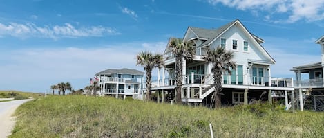 A beachfront property with multiple-story houses, a sandy path, and palm trees.